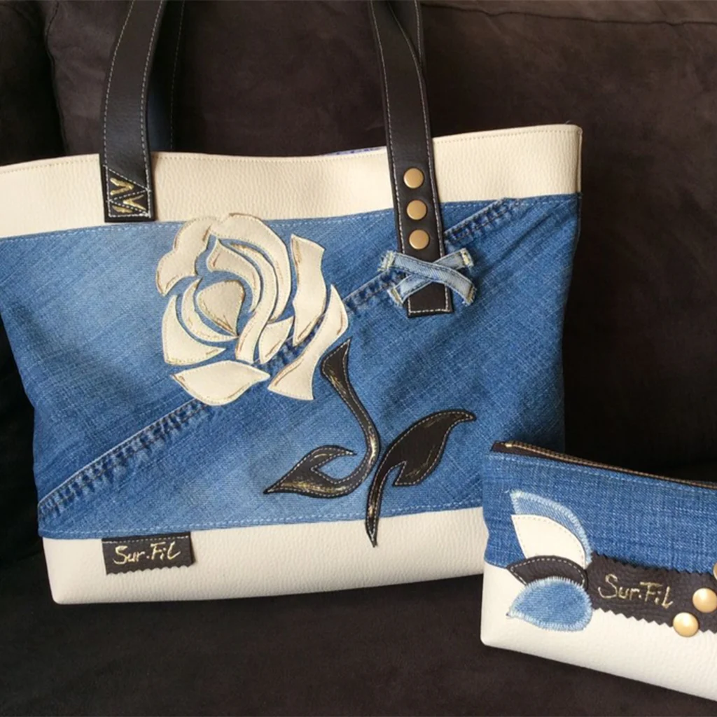 Sac cabas artisanal en jean recyclé et simili cuir blanc cassé, décoré d'une fleur stylisée en appliqué, accompagné d'une trousse assortie.