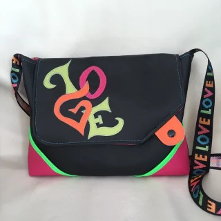 Sac bandoulière noir en simili cuir, décoré d’un appliqué multicolore “LOVE” et d’une sangle arc-en-ciel assortie, avec détails fluo rose et vert.