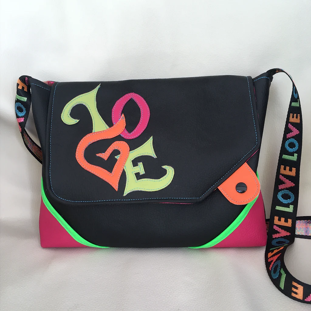 Sac bandoulière noir en simili cuir, décoré d’un appliqué multicolore “LOVE” et d’une sangle arc-en-ciel assortie, avec détails fluo rose et vert.
