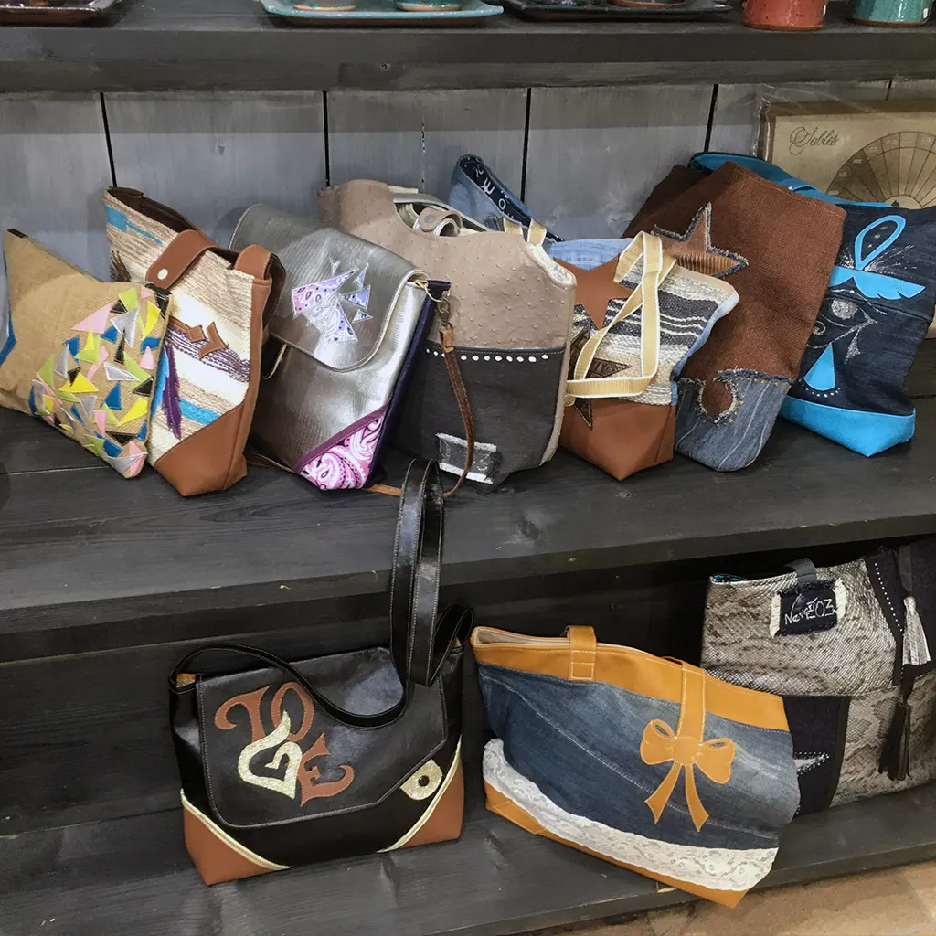 Étagère en bois foncé présentant une collection de sacs à main artisanaux KerdeL en jute, jean, simili cuir, wax et suédine, ornés d’appliqués colorés et de détails cousus main.